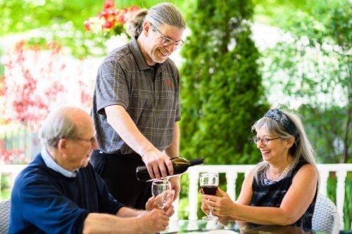 Innkeeper Chuck Pappalardo of Kingsley House pours a red wine into the glasses of two guests seated on the front porch of this B&B near a winery.