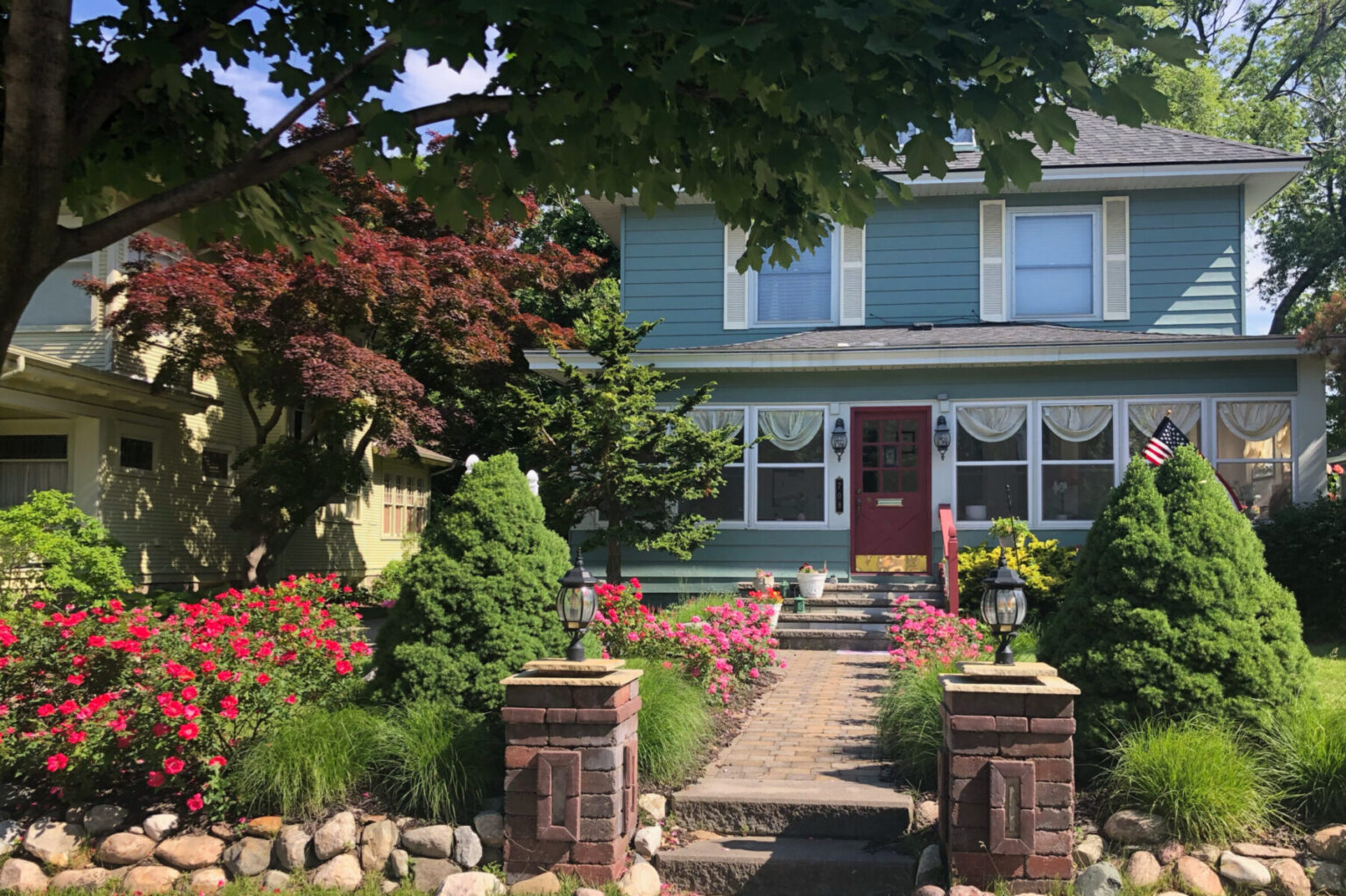 Four square blue building with walkway surrounded by pink flowers at the Candlelite Inn B&B in Ludington