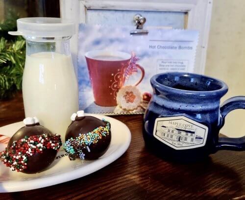 Hot chocolate “bombs” on a plate next to mugs and milk