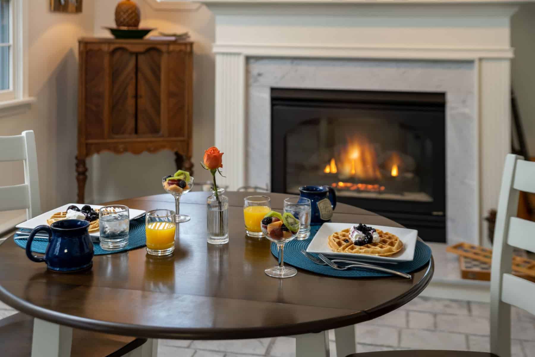 Breakfast setting for two inside at House on the Hill Bed and Breakfast with fireplace in the background and featuring Waffles