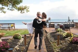 Groom carrying his bride with lake views and blue skies at the Huron House