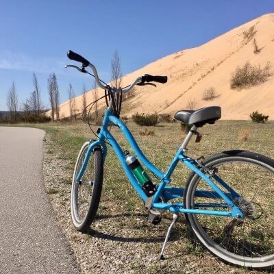 Blue bike stands along paved trail with Sleeping Bear Dunes in background.