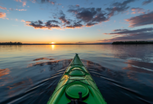 Front of a green kayak on a lake at sunset