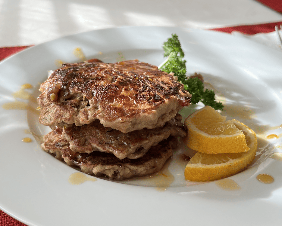 Three oatmeal pancakes on a white plate with an orange slice