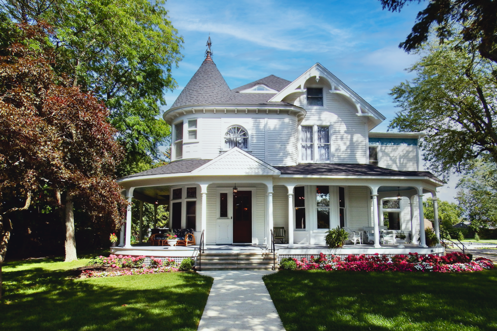 Victorian white two story building with wrap around porch and summer flowers