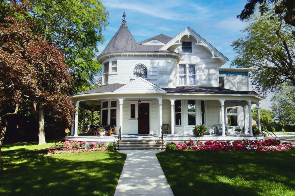 Victorian white two story building with wrap around porch and summer flowers