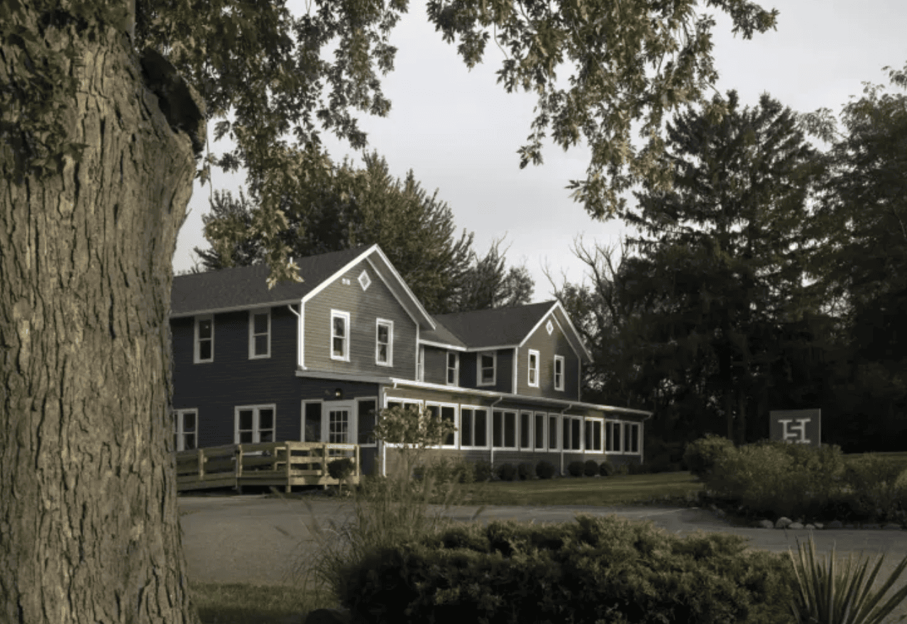 Side view of the Hotel Saugatuck painted grey with white trim with a tree on the side