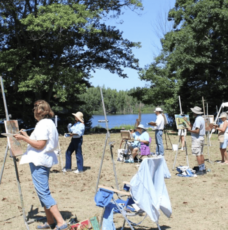 Artists with easels on a beach with water in the background