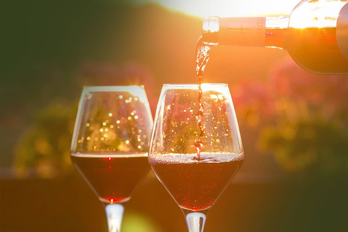 two glasses of red wine being filled with sunset in the background