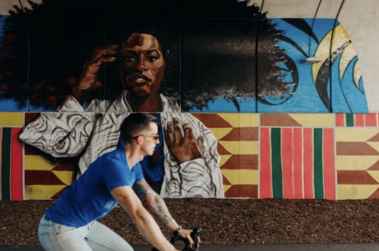 Man in a blue shirt riding by wall art in Detroit