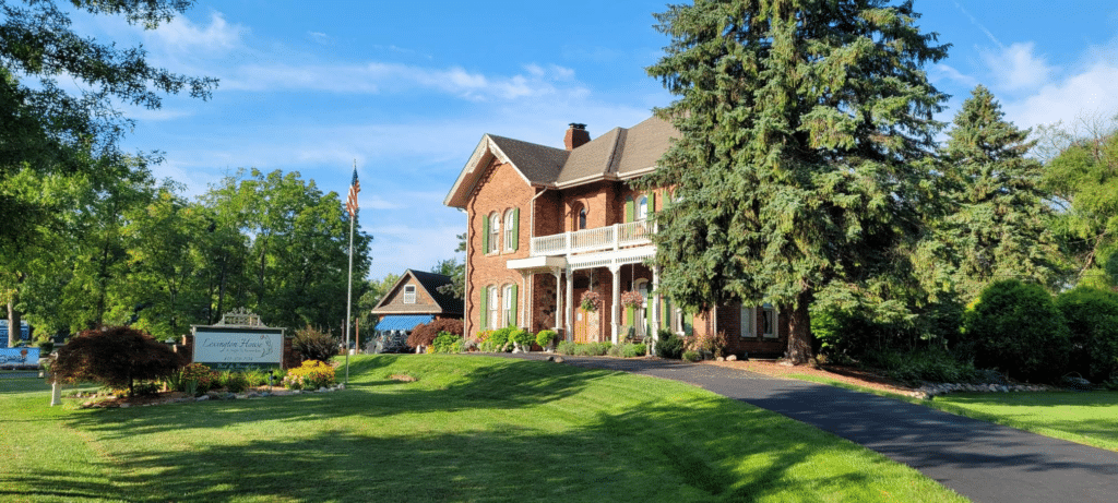 The two story red brick Lexington House B&B in Lexington, Michigan with large pine trees flanking the building