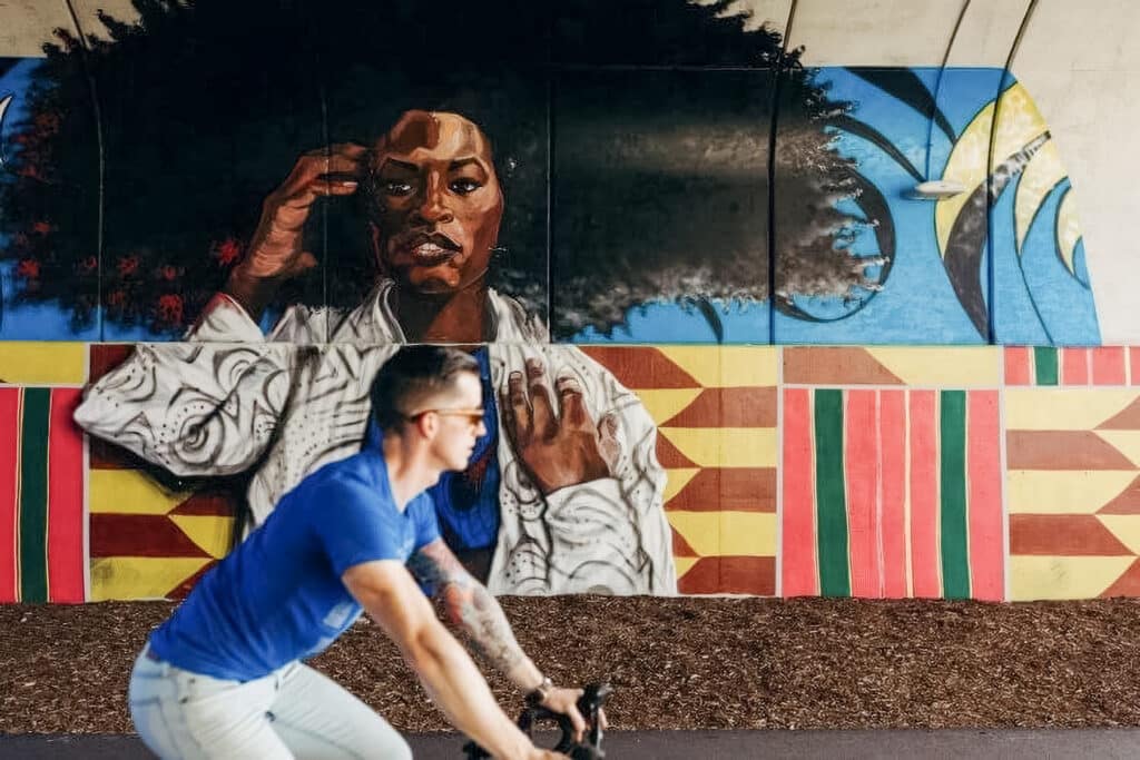 Young man writing a bike in Detroit with an artwork mural behind