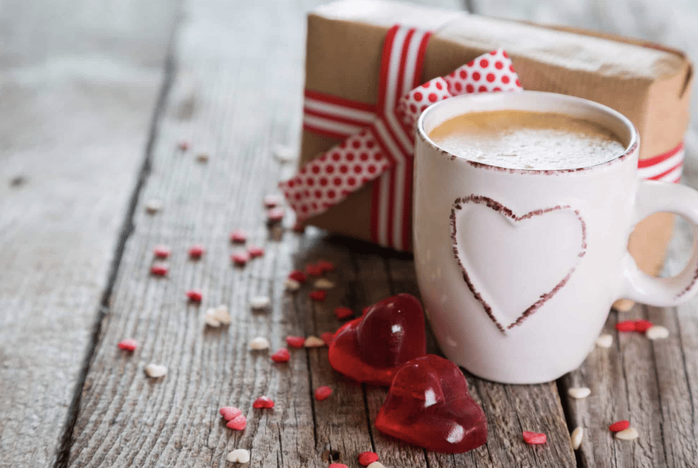 White cup of cocoa with a box wrapped with red ribbon